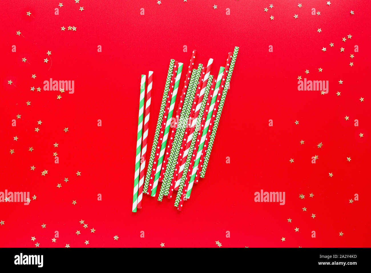 Striped drink straws of different colors on red background. New Year or Christmas pattern. Minimalism concept. Pop art style. Top view, Flat lay with Stock Photo