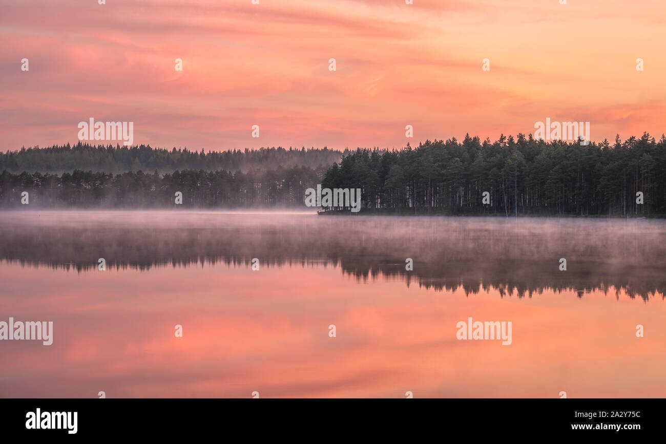 Beautiful sunrise landscape with misty mood and calm lake at foggy summer morning in Finland Stock Photo