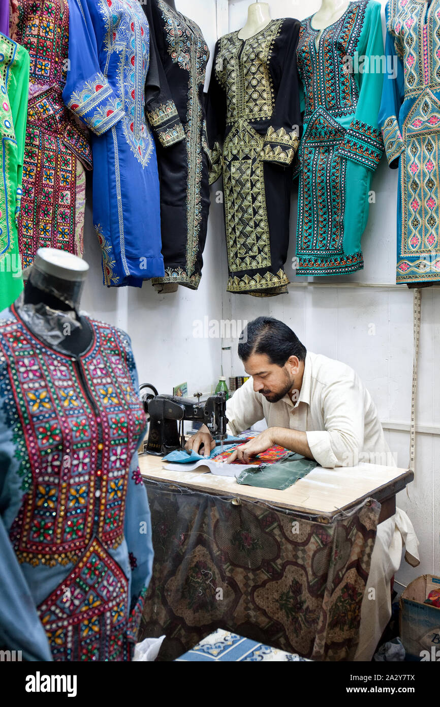A tailor in his shop sitting in front at a sewing machine with colorful