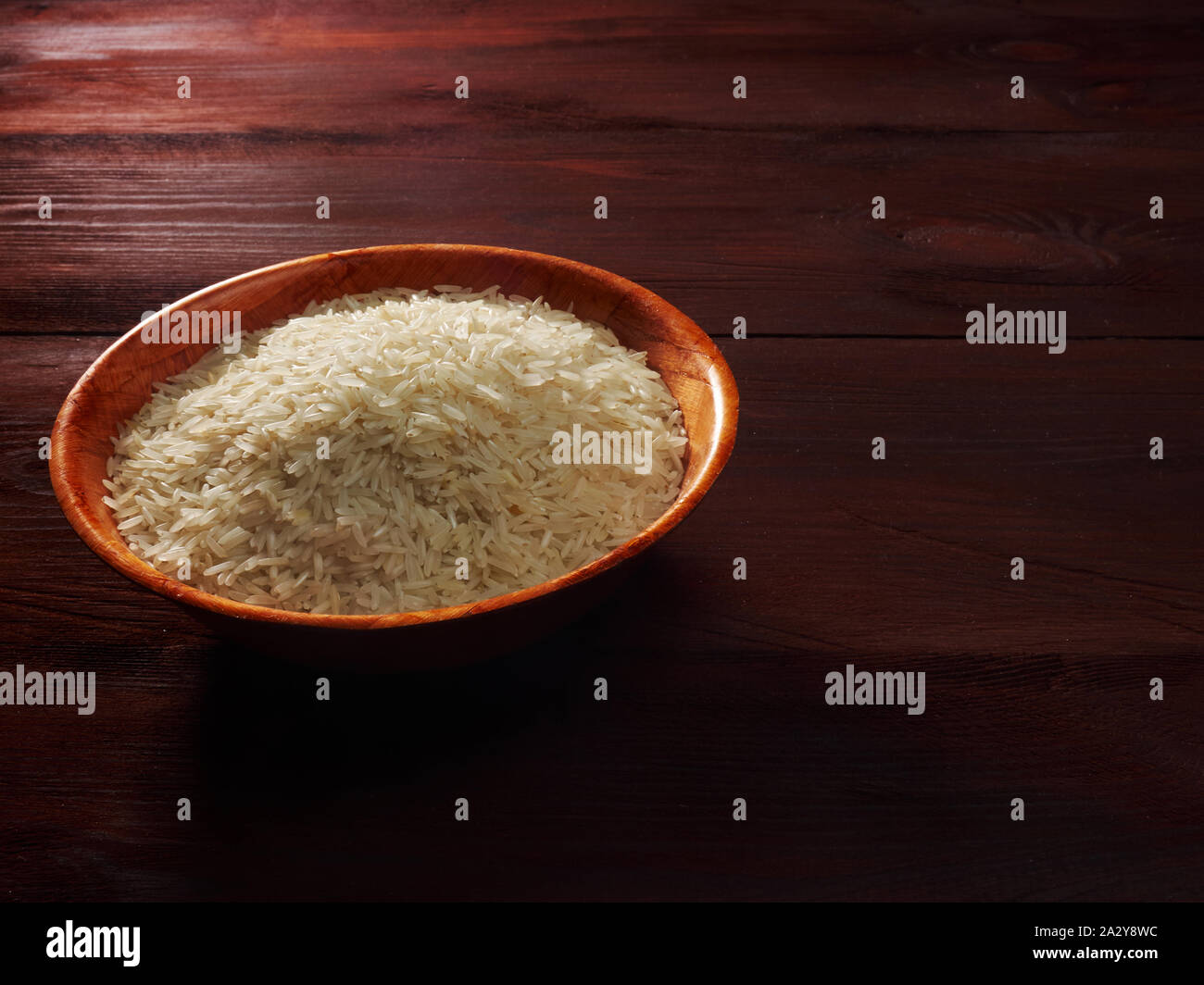 White basmati rice in a bamboo bowl on a brown wooden background Stock Photo
