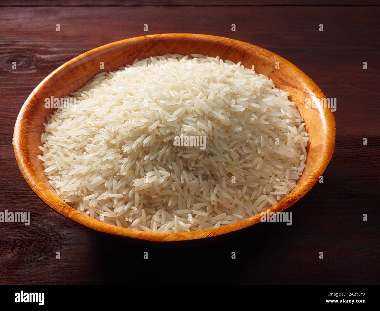 White basmati rice in a bamboo bowl on a brown wooden background Stock Photo