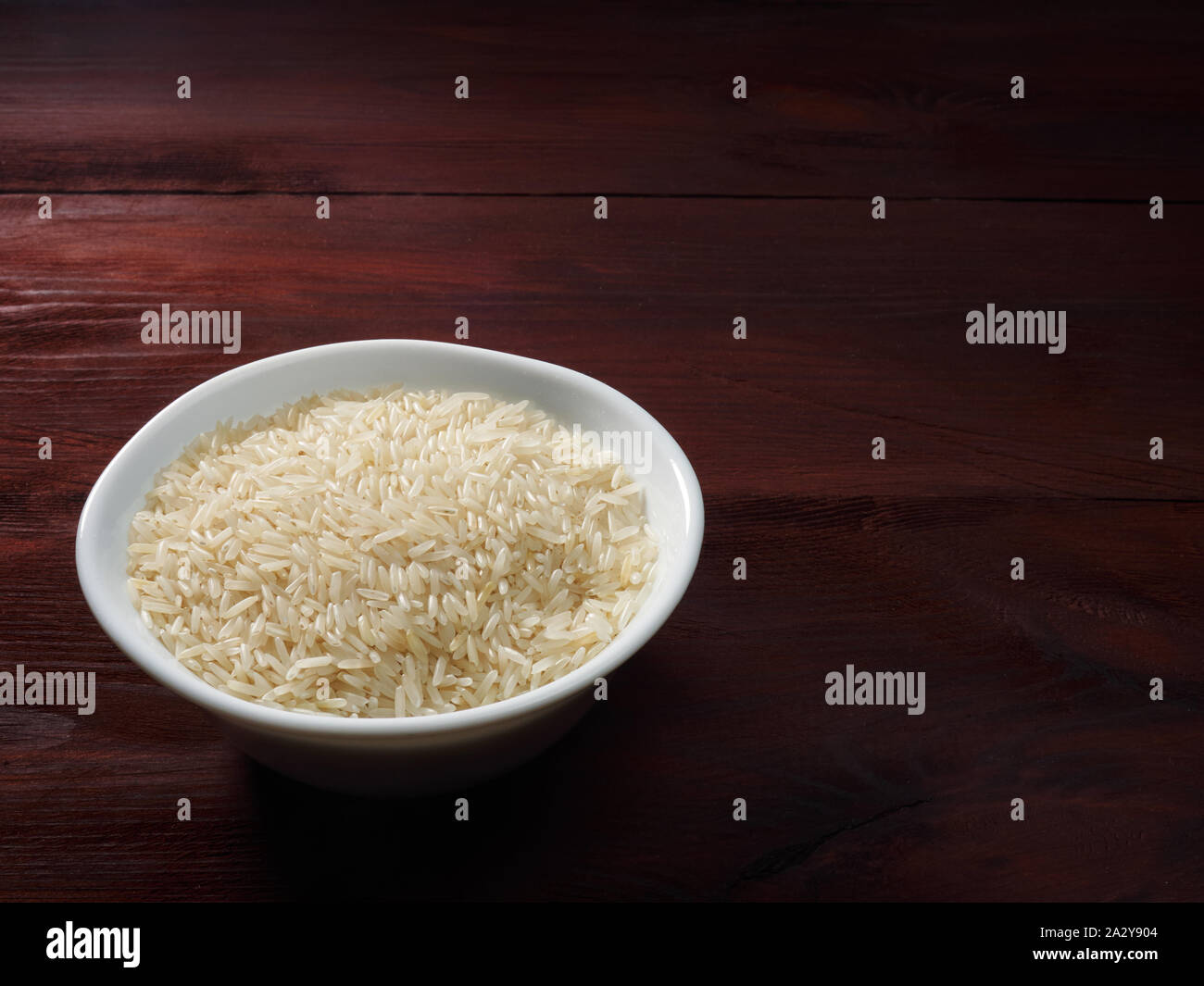 Raw Basmati rice in a white bowl on a brown wooden background Stock Photo