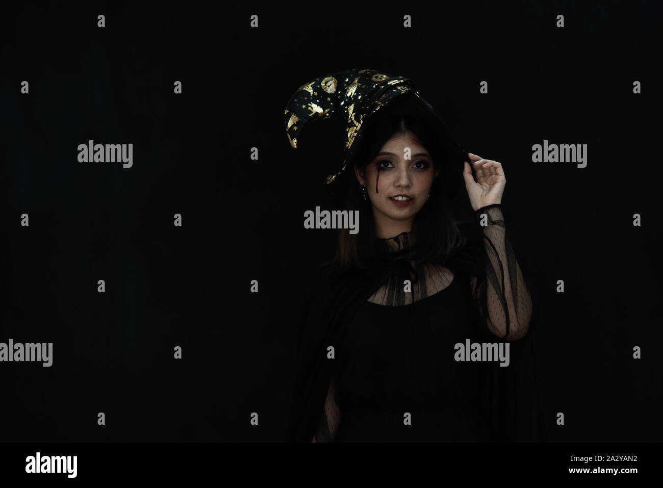 An Asian beautiful woman model dressed as a witch and a witch's hat costume smile and acting on Halloween party with dark background. copy space Stock Photo