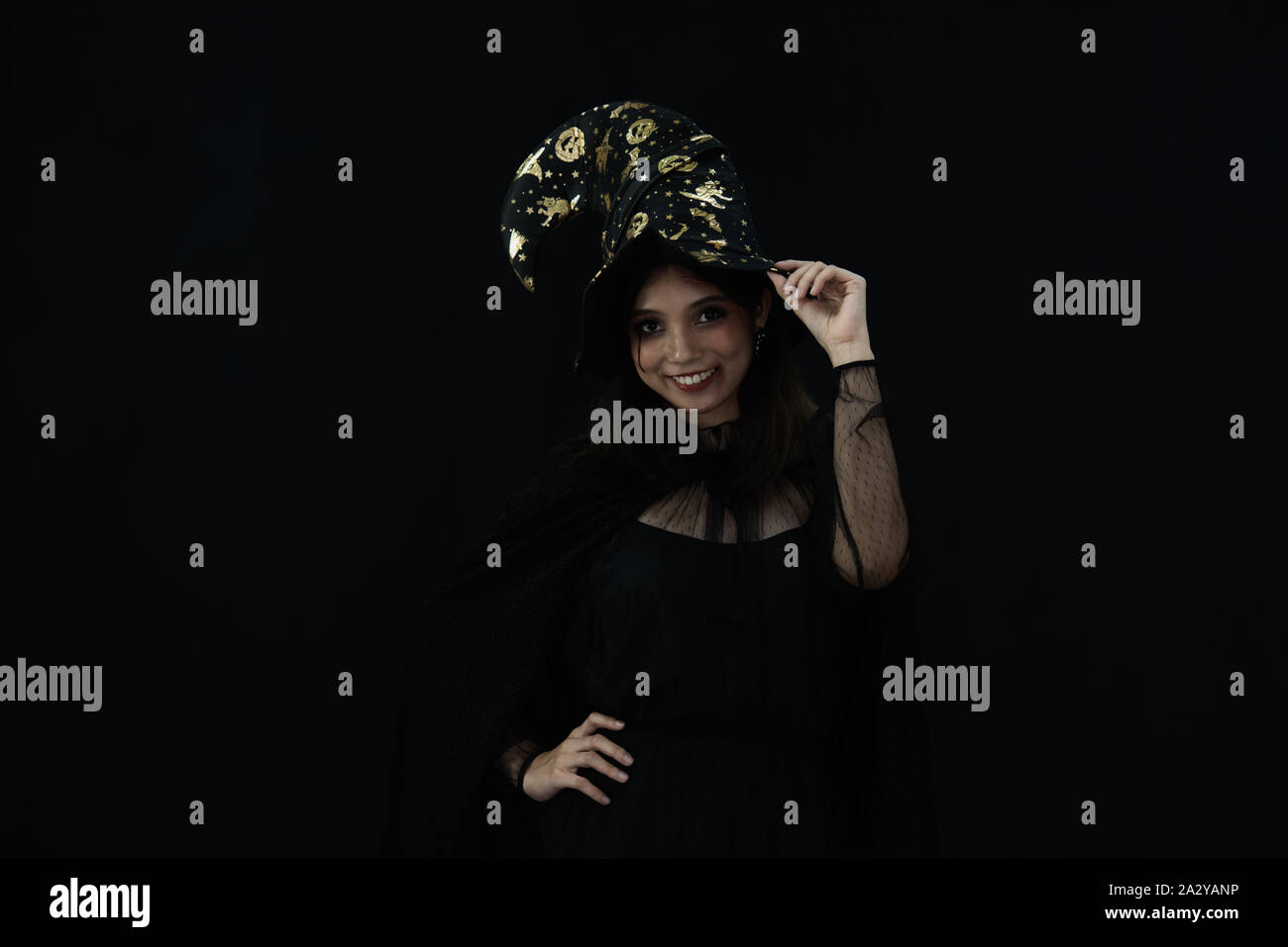 An Asian beautiful woman model dressed as a witch and a witch's hat costume smile and acting on Halloween party with dark background. copy space Stock Photo