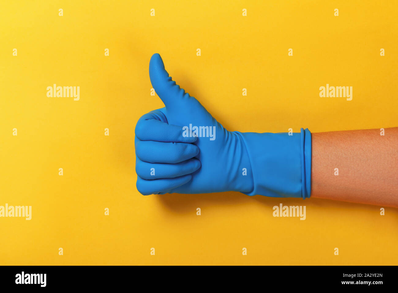 Thumb up in a blue protective glove on a yellow background. Stock Photo