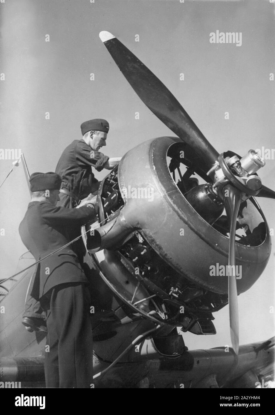 Airplane engineers.Three mechanics are performing the important last minute check of engine details before start. The airplane is a swedish single propeller engine light bomb and survaillance unit model B5. The swedish company Saab Svenska Aeroplan AB produced this airplane on license from American Northrop and their model 8A-1.  Picture taken in the 1940s during the second world war. Stock Photo