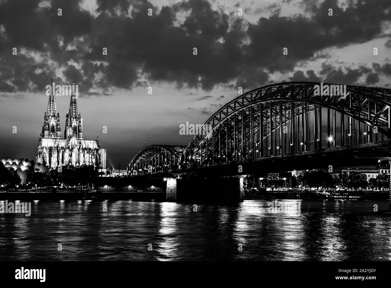 Cologne, Germany: Beautiful black and white night landscape of the gothic cathedral, Hohenzollern Bridge and reflections over the River Rhine with clo Stock Photo