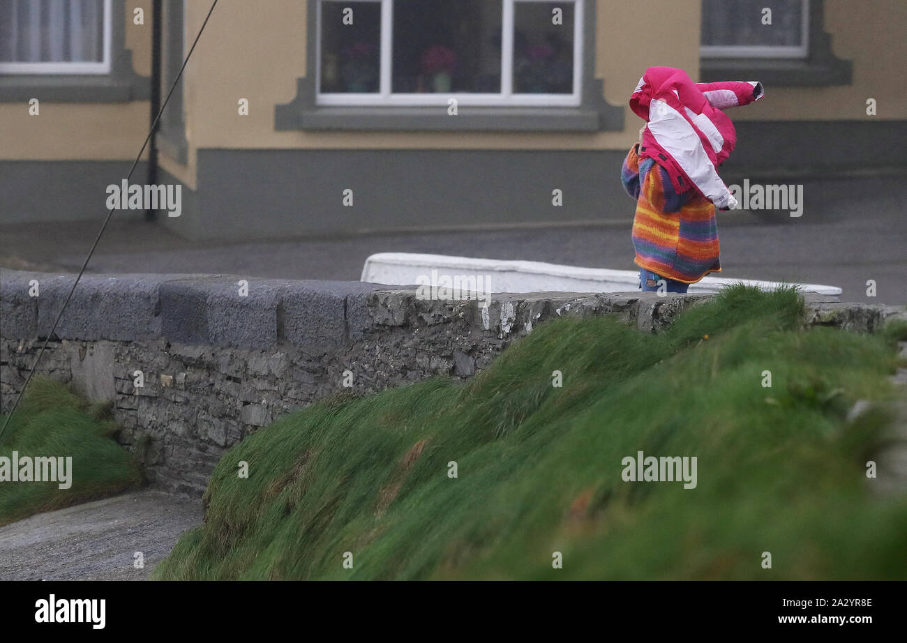 A woman struggles with her coat along the sea front in Lahinch, County Clare, on the West Coast of Ireland as thousands of homes and businesses have been left without power as Storm Lorenzo passed across Ireland. Stock Photo