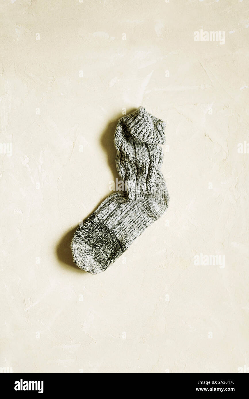 Handmade warm knitted sock grey color on textured background with copy space.Winter and autumn concept of eco clothes.Minimalism Kinfolk Style Stock Photo