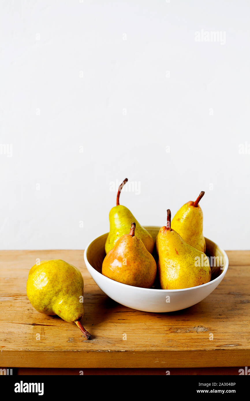 Organic yellow pears in white bowl on old wooden table and white wall background with copy space.Rural minimalistic still life.Kinfolk style Stock Photo