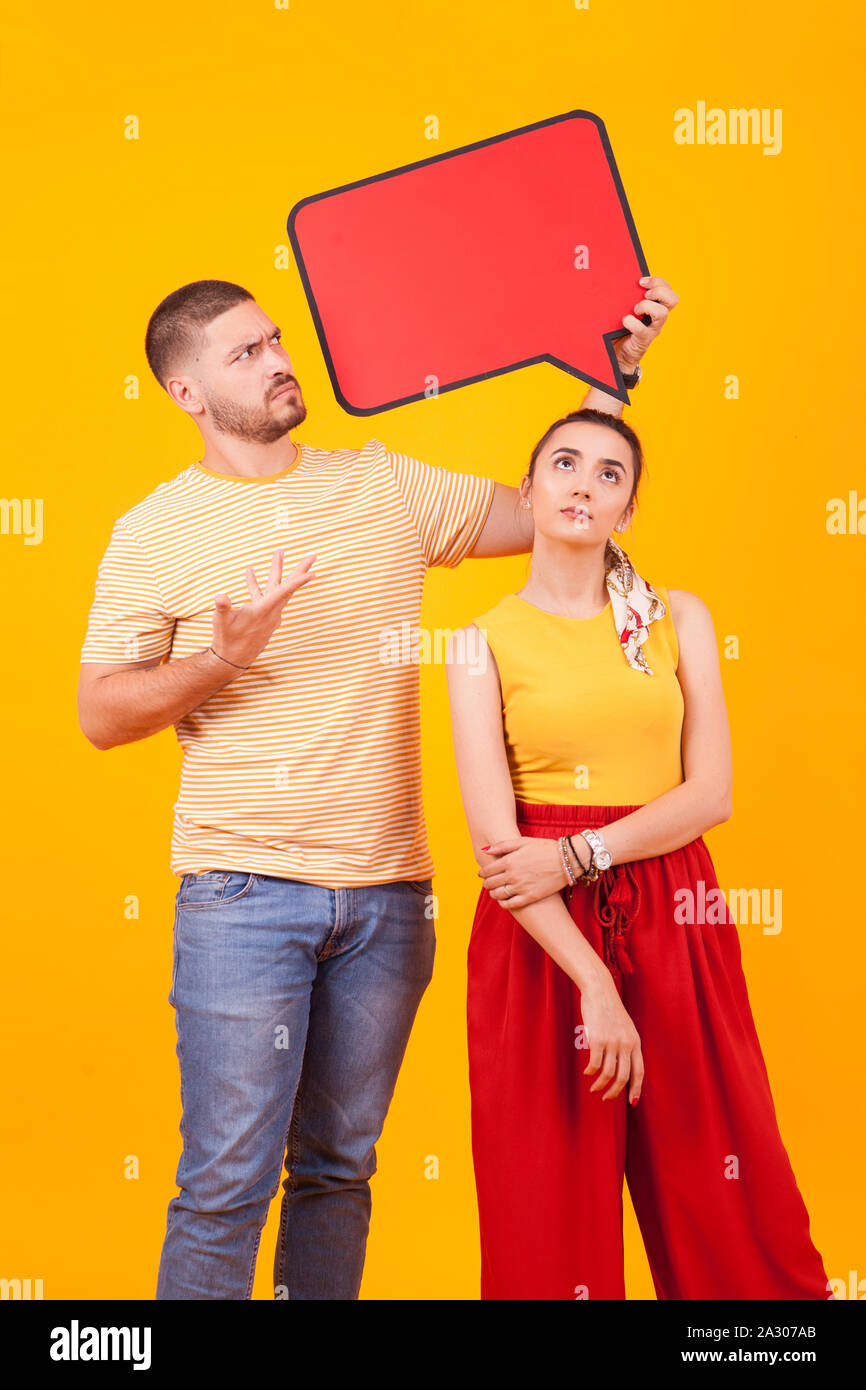 Confused boyfriend pointing at bubble thought and girlfriend looking up. Stock Photo