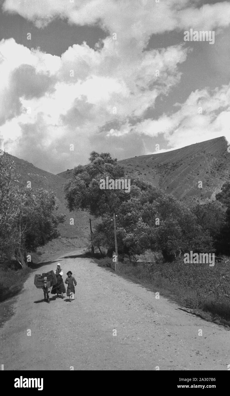 1930s, historical, Yugoslavia, mother with daughter and their donkey walking along a rural mountain road. The multi-national state came into being in 1918 and the formation of the Kingdom of Serbs, Croats and Slovenes, commonly known as Yugoslavia, dominated by three main mountain regions, including the Dinaric Alps of the Balkan peninsula. Stock Photo