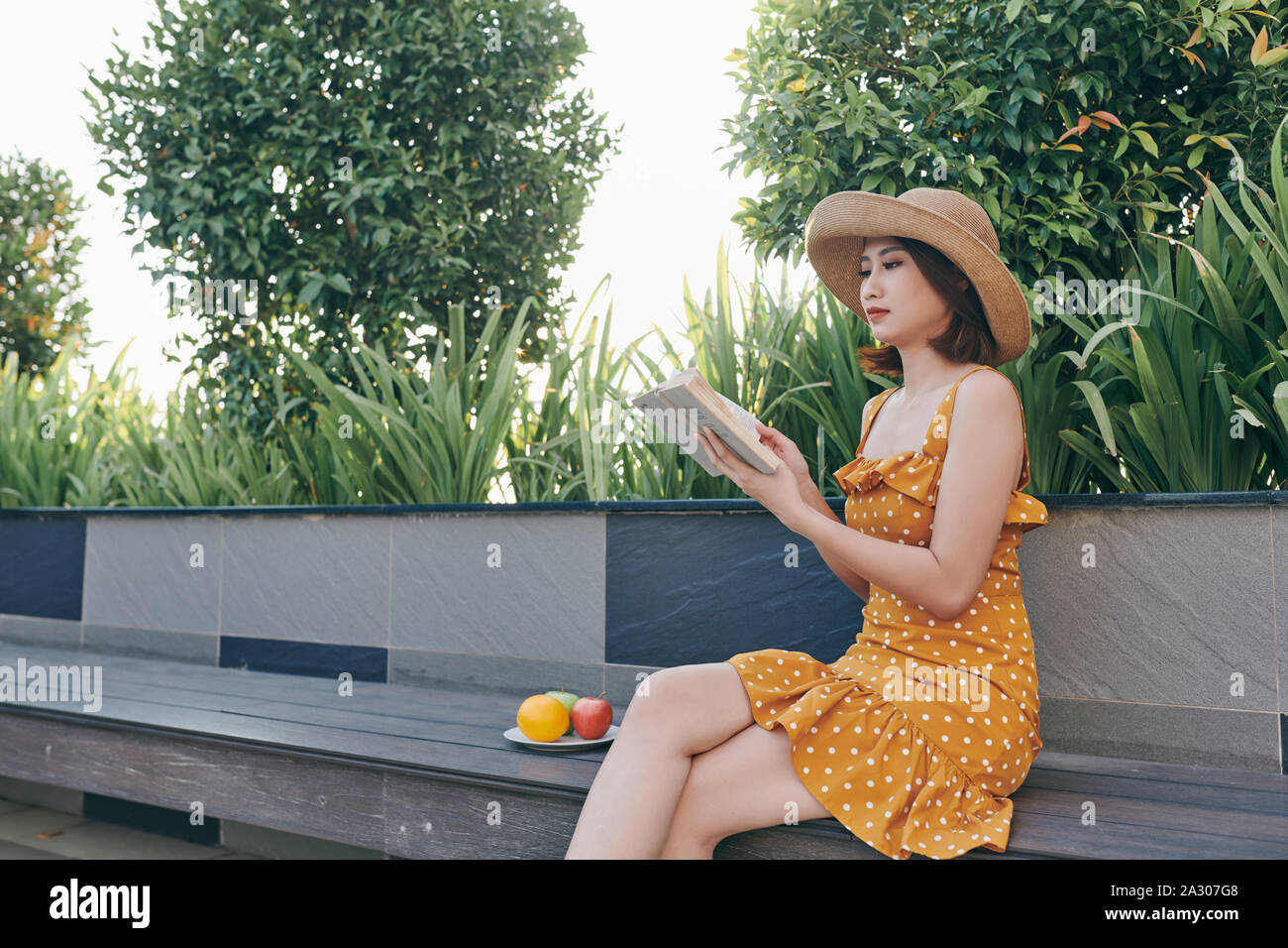 Cute young woman sitting in the park and reading the book Stock Photo ...