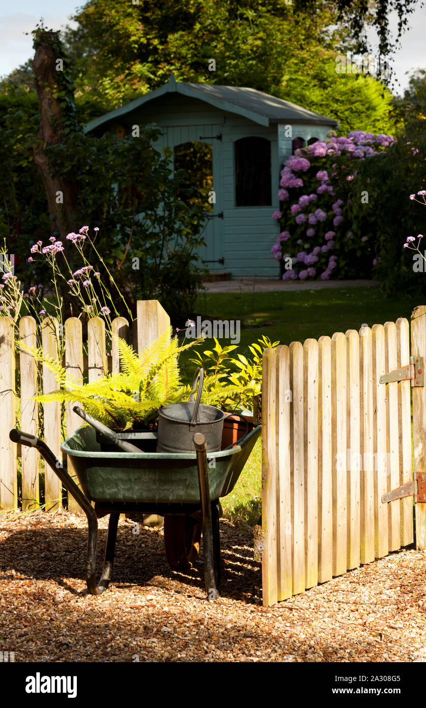 A wheelbarrow full of plants entering a garden through a wooden gate Stock Photo