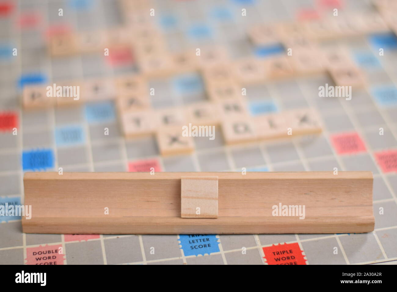 1 blank wooden scrabble tile on a tile-rack, for you to fill in your own word. In the background a vintage board, out of focus, with copy space Stock Photo