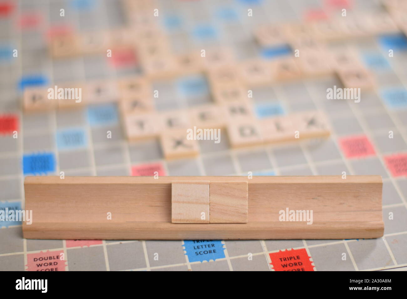 2 blank wooden scrabble tiles on a tile-rack, for you to fill in your own word. In the background a vintage board, out of focus, with copy space Stock Photo