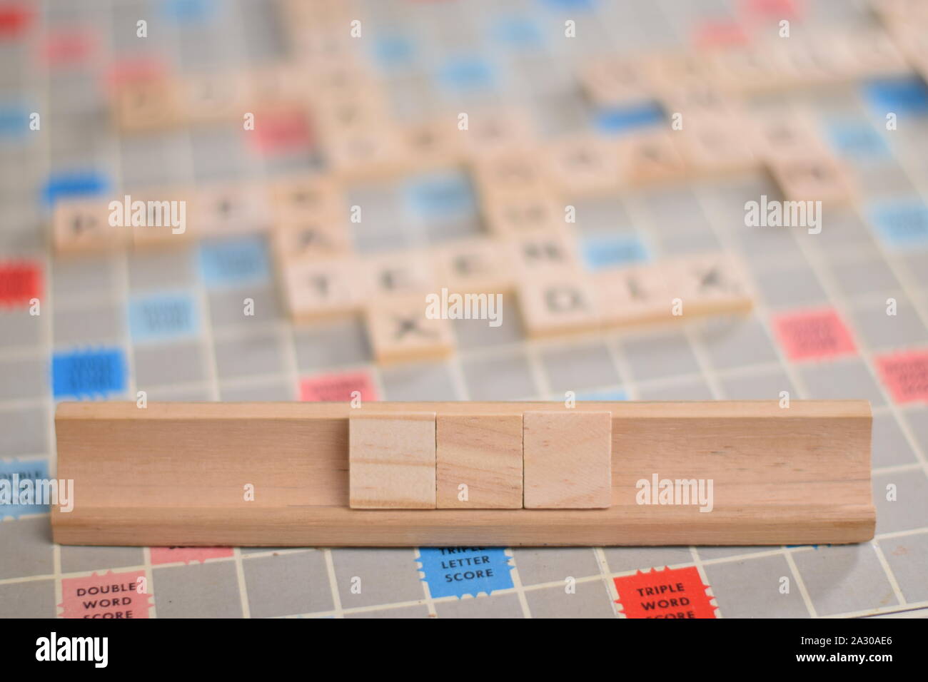 3 blank wooden scrabble tiles on a tile-rack, for you to fill in your own word. In the background a vintage board, out of focus, with copy space Stock Photo