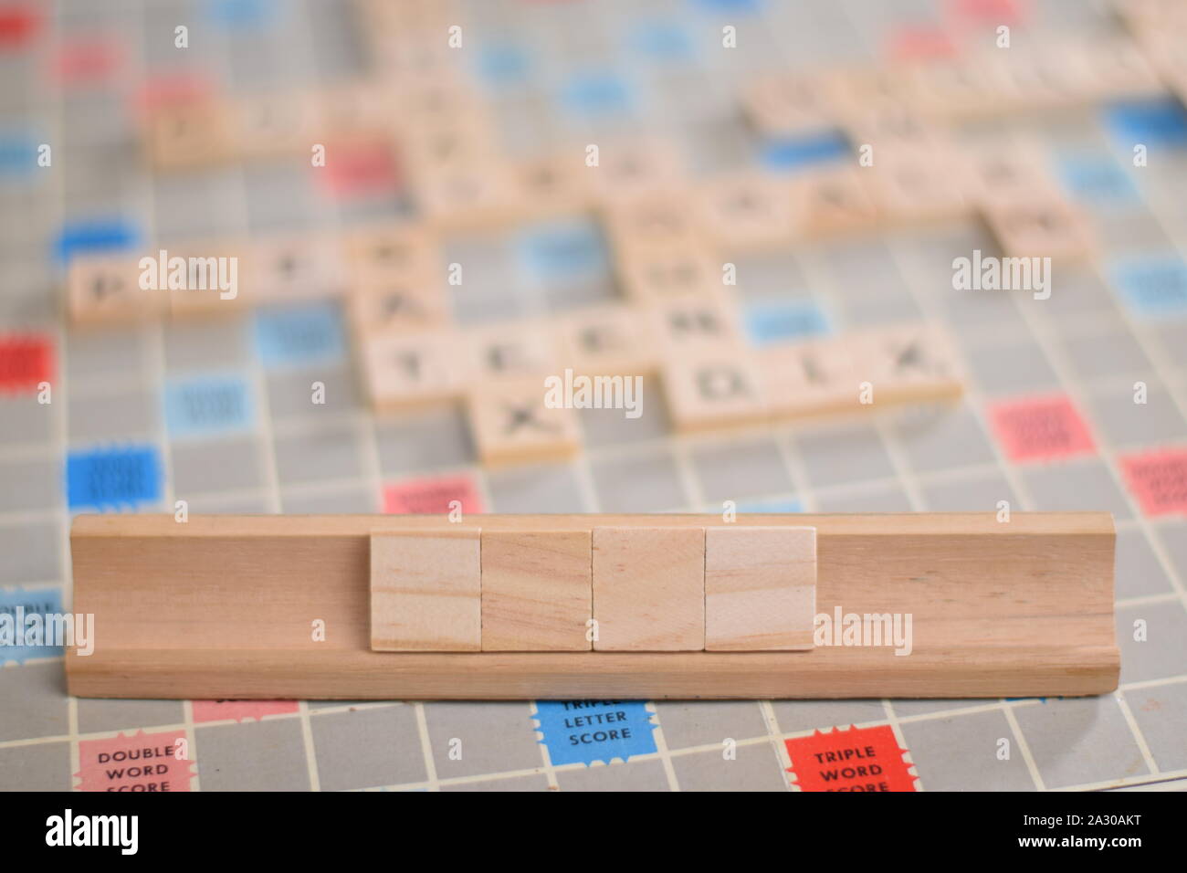 4 blank wooden scrabble tiles on a tile-rack, for you to fill in your own word. In the background a vintage board, out of focus, with copy space Stock Photo