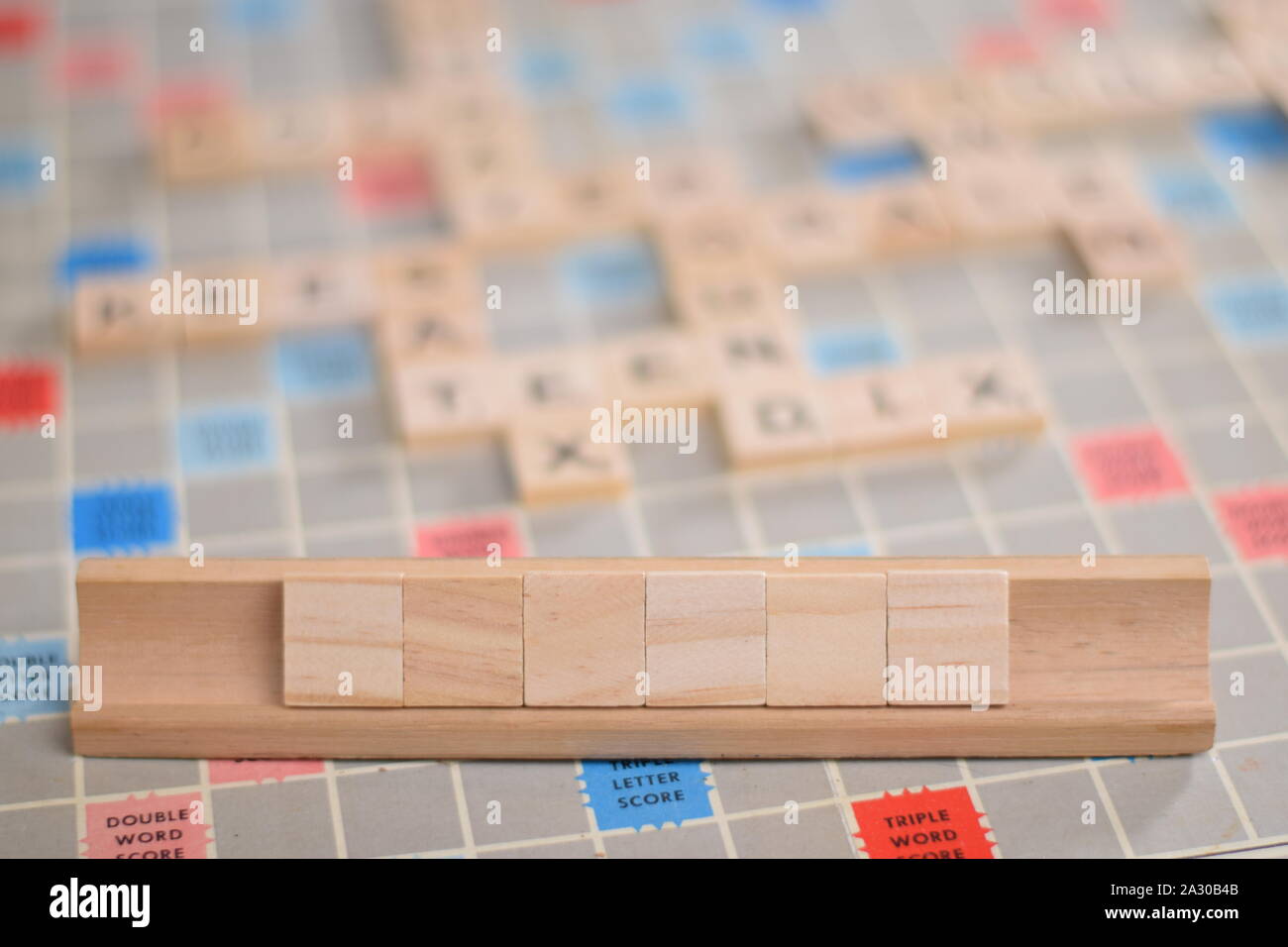 6 blank wooden scrabble tiles on a tile-rack, for you to fill in your own word. In the background a vintage board, out of focus, with copy space Stock Photo