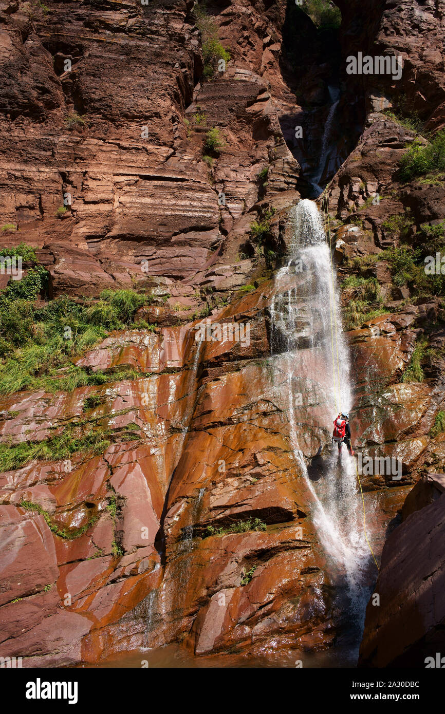 Young man abseiling a waterfall in a red rock formation. Clue d'Amen, Gorges de Daluis, Guillaumes, Alpes-Maritimes, France. Stock Photo