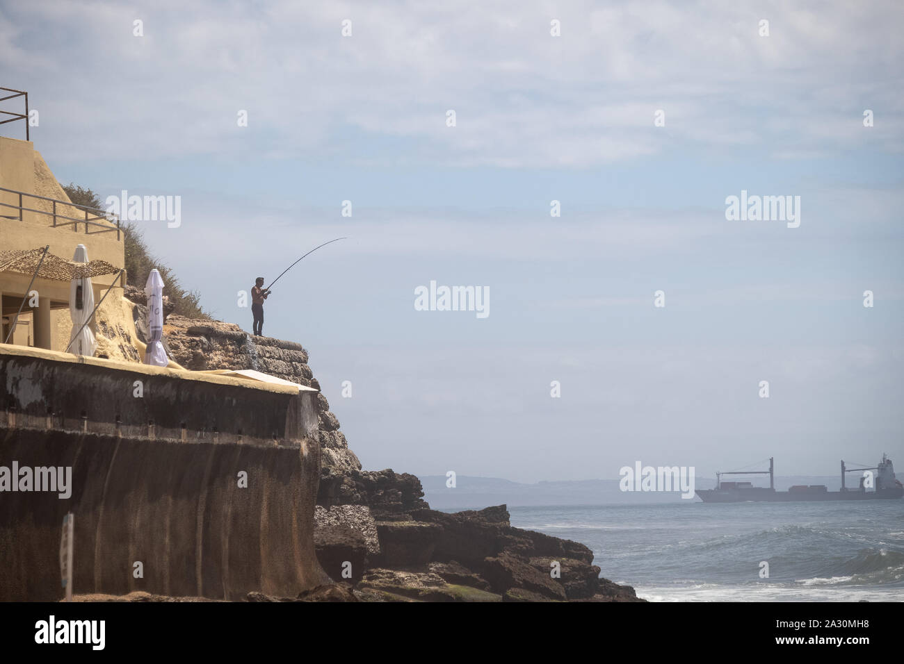 Coast of Portugal, Parede district. Ocean landscape, a man fishing, waves crashing against the rocks. Stock Photo