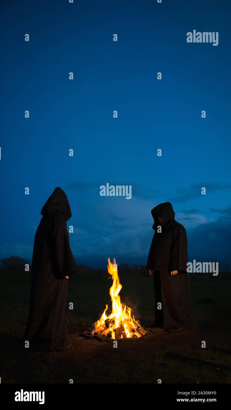 Mysterious, hooded, Pagan figures wearing hoods and cloaks worshiping gods around a fire in a ceremonial ritual at night with copy space Stock Photo