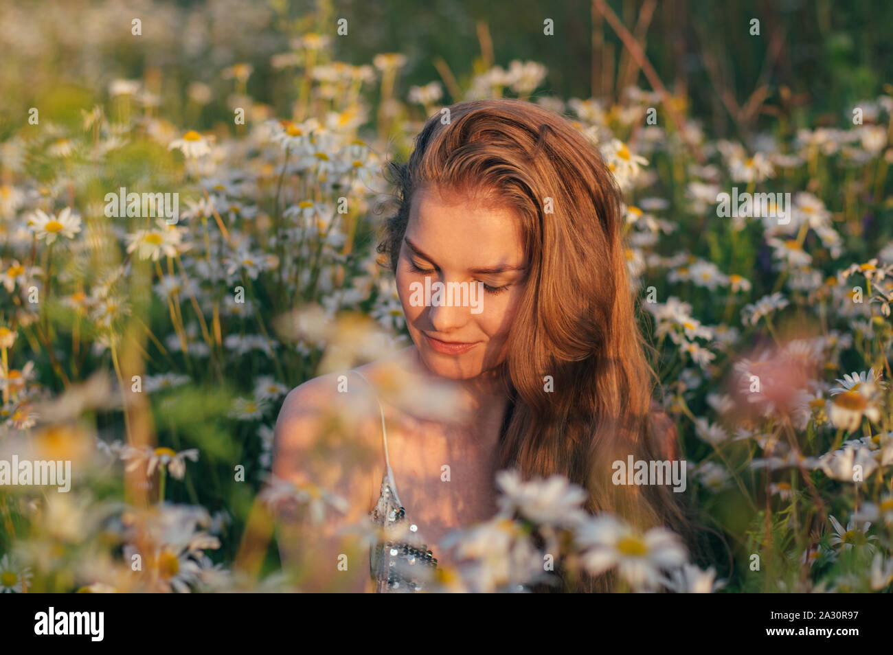 Portrait of pretty blond woman with closed eyes sitting in chamomile ...