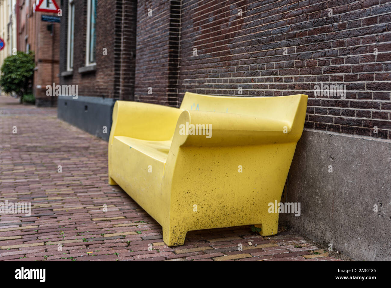 yellow bench canape as street furniture in the street against a brick wall on a brick pavement Stock Photo
