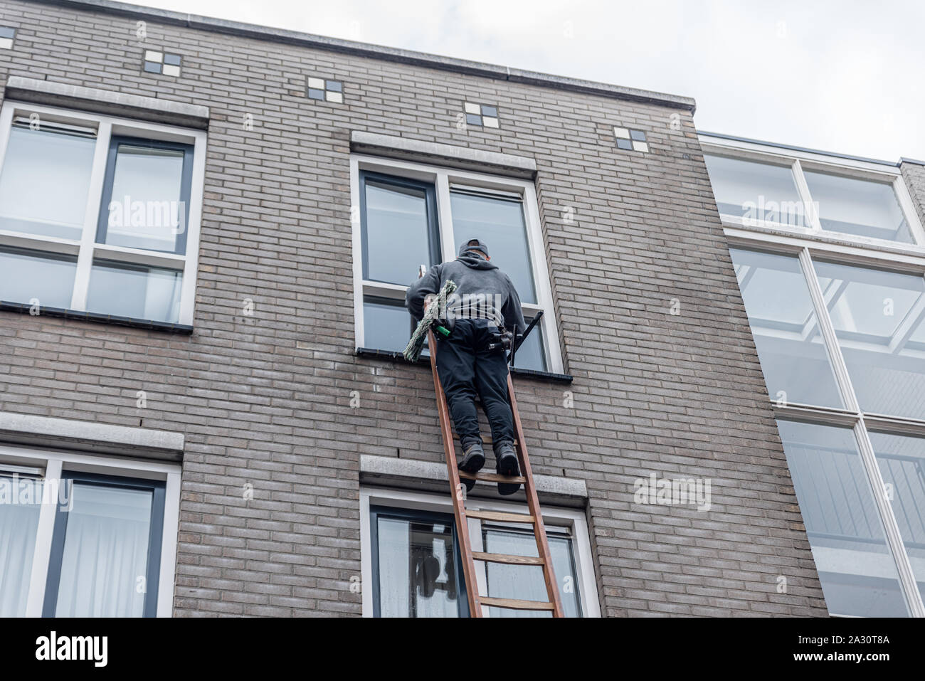 Window cleaner on a ladder cleaning the windows high against a building of brick walls. Stock Photo