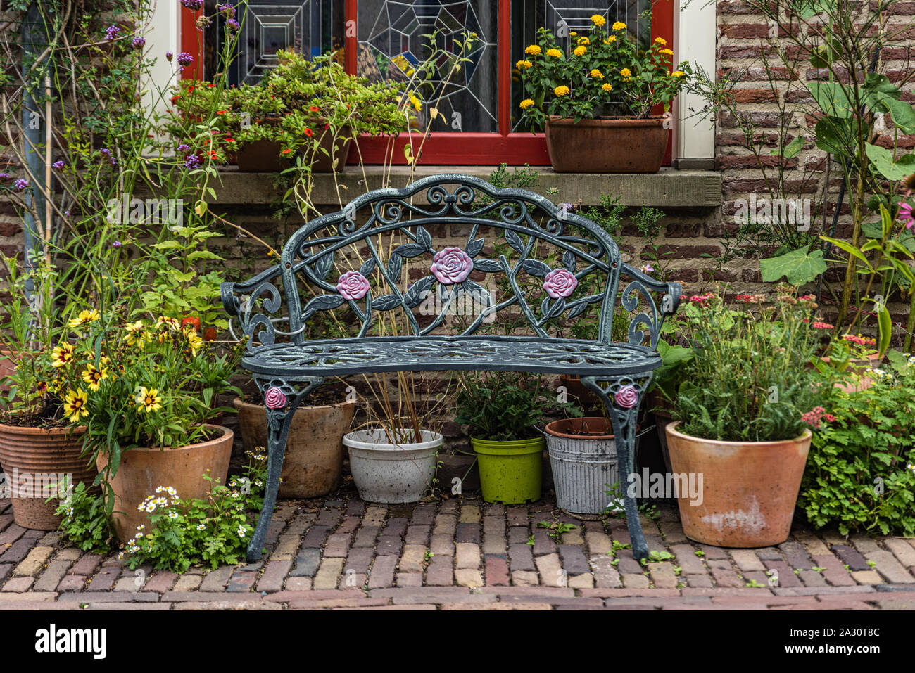 Romantic roses bench in front of a lovely house with a lot of pot plants and flowers around it making a lovely romantic scene Stock Photo