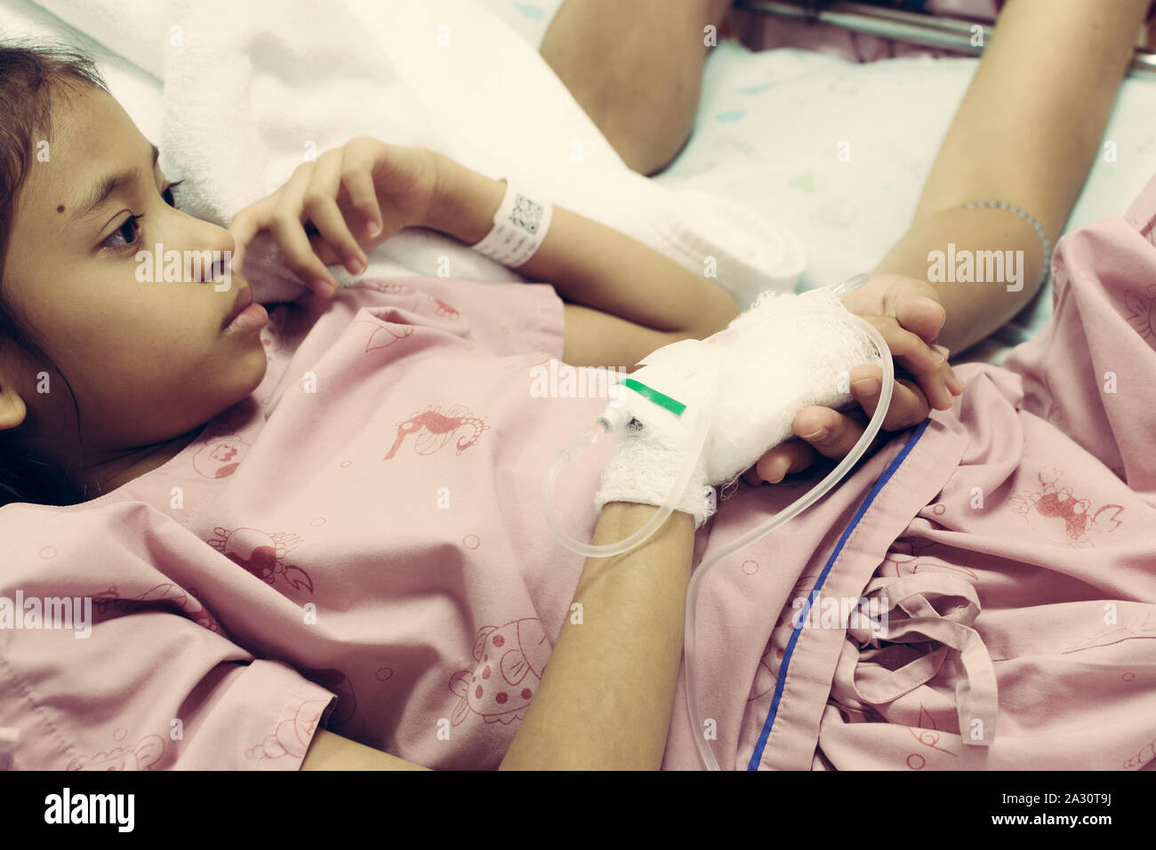 Young daughter sick in hospital and her hand is holding by her mother with care Stock Photo