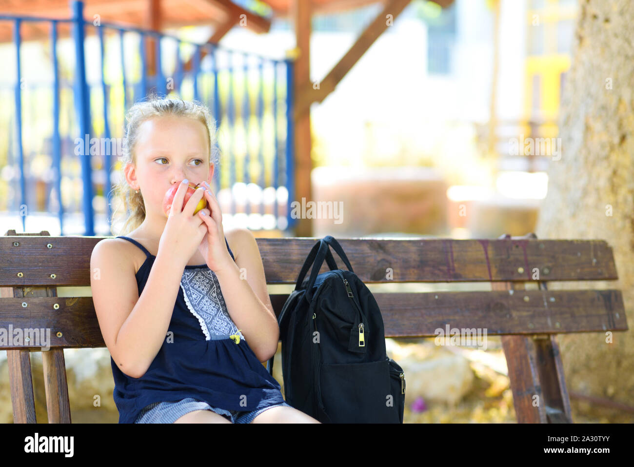 Little girl is eating an apple. Healthy nutrition. Pretty child eating an apple at park , nature outdoors. Teenager pupil enjoying healthy lunch in schoolyard. Stock Photo