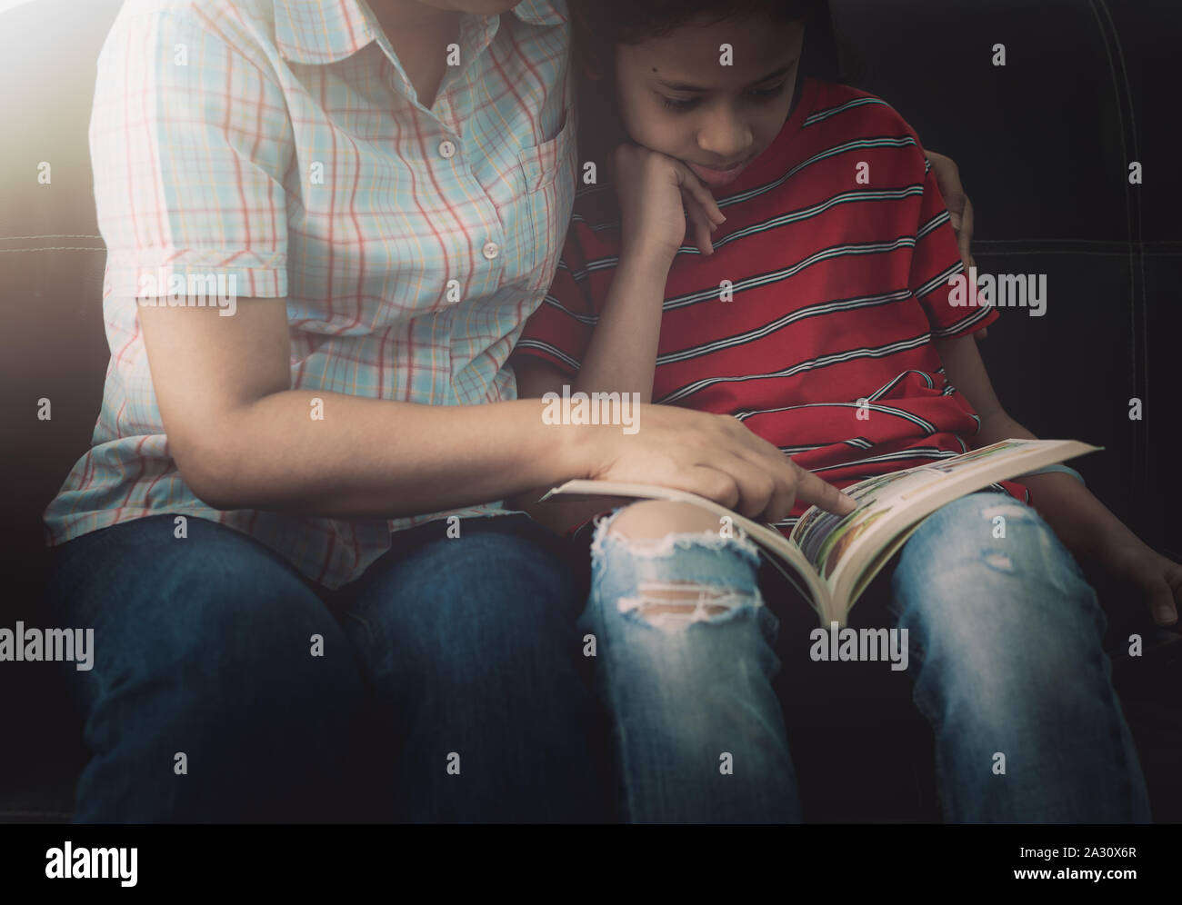 Mother and daughter reading book and having fun while spending time together at home under the warm light. Stock Photo
