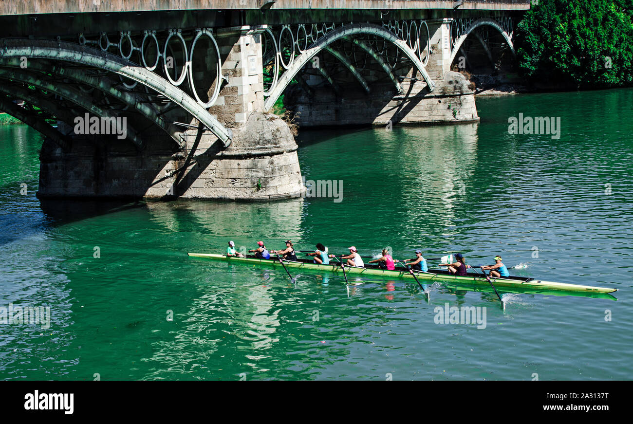 Group of women rowing in the Guadalquivir river under the Triana Bridge, Seville, Andalusia, Spain Stock Photo