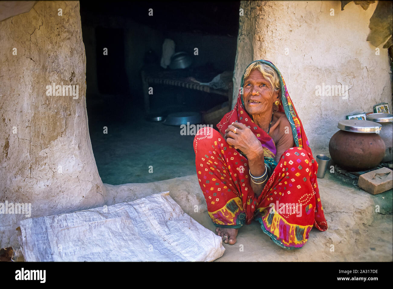 An elderly Indian woman sitting in front of the entrance to her mud hut ...