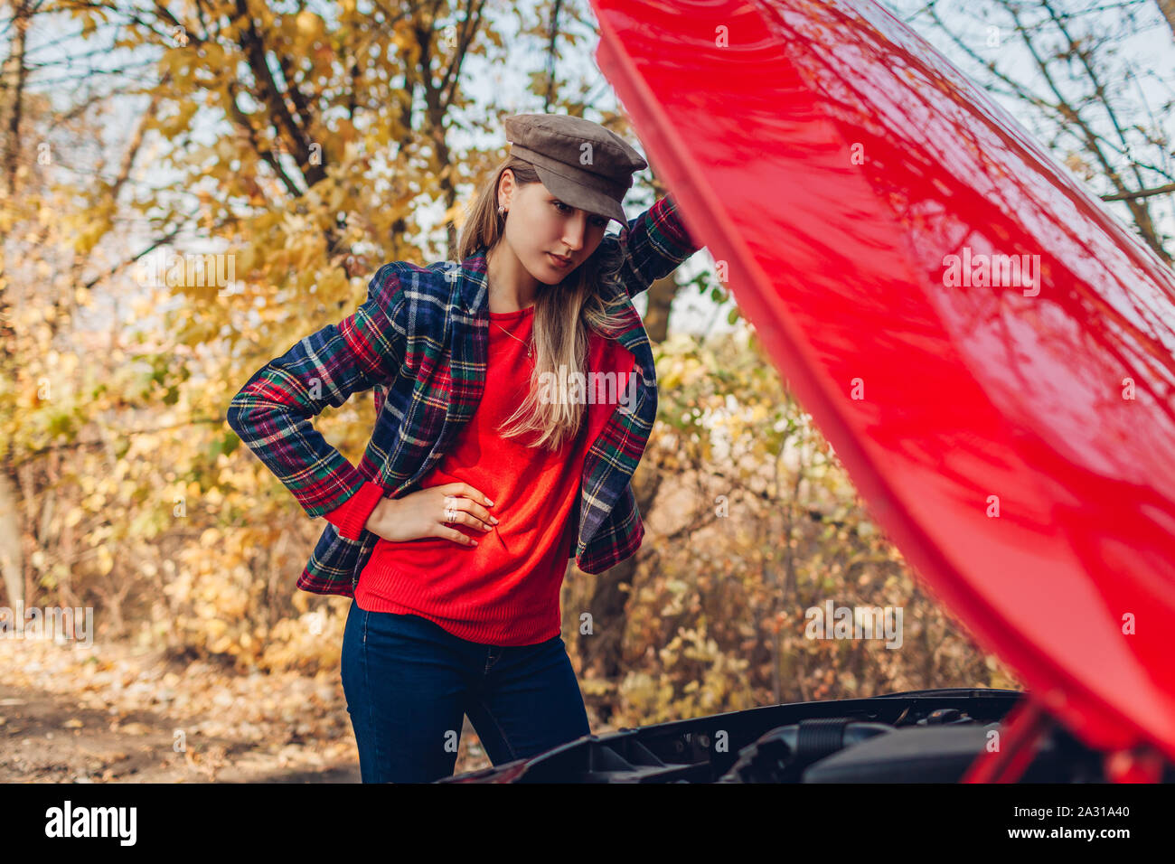 Broken car. Sad woman opening hood of her auto that stopped on road outdoors. Breakage Stock Photo