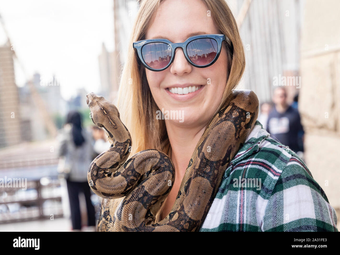 Young, twenties female tourist with a large snake around her neck on the Brooklyn Bridge in New York City, USA. Stock Photo
