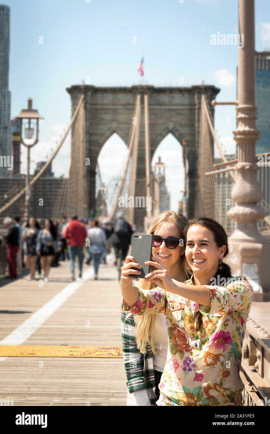Two twenty year old female tourists take selfies on the Brooklyn Bridge ...