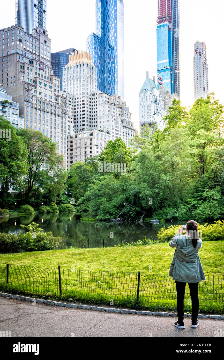Young woman tourist photographs pond and buildings in Central Park, New York City, USA. Stock Photo