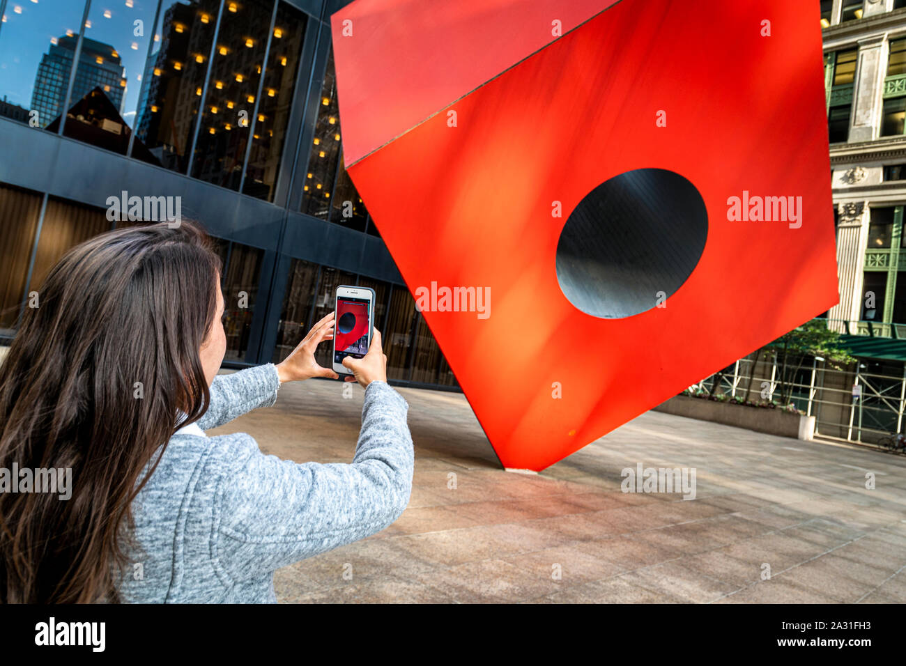 Young woman tourist photographs Isamu Noguchi's iconic Red Cube in Lower Manhattan, New York City, USA. Stock Photo