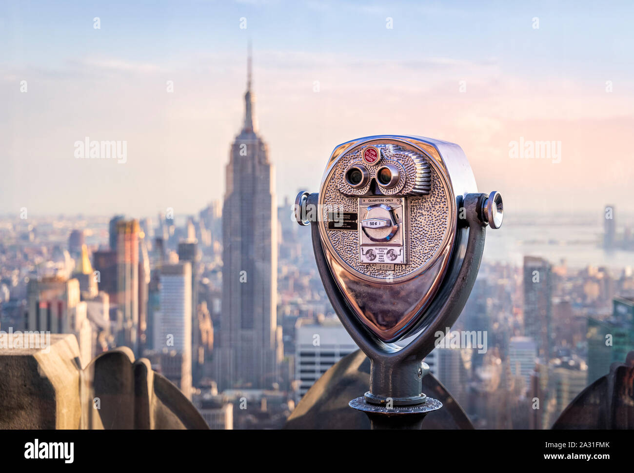 One of the iconic telescopes on Top of the Rock Observatory with the Empire State Building in the distance, New York City, USA. Stock Photo