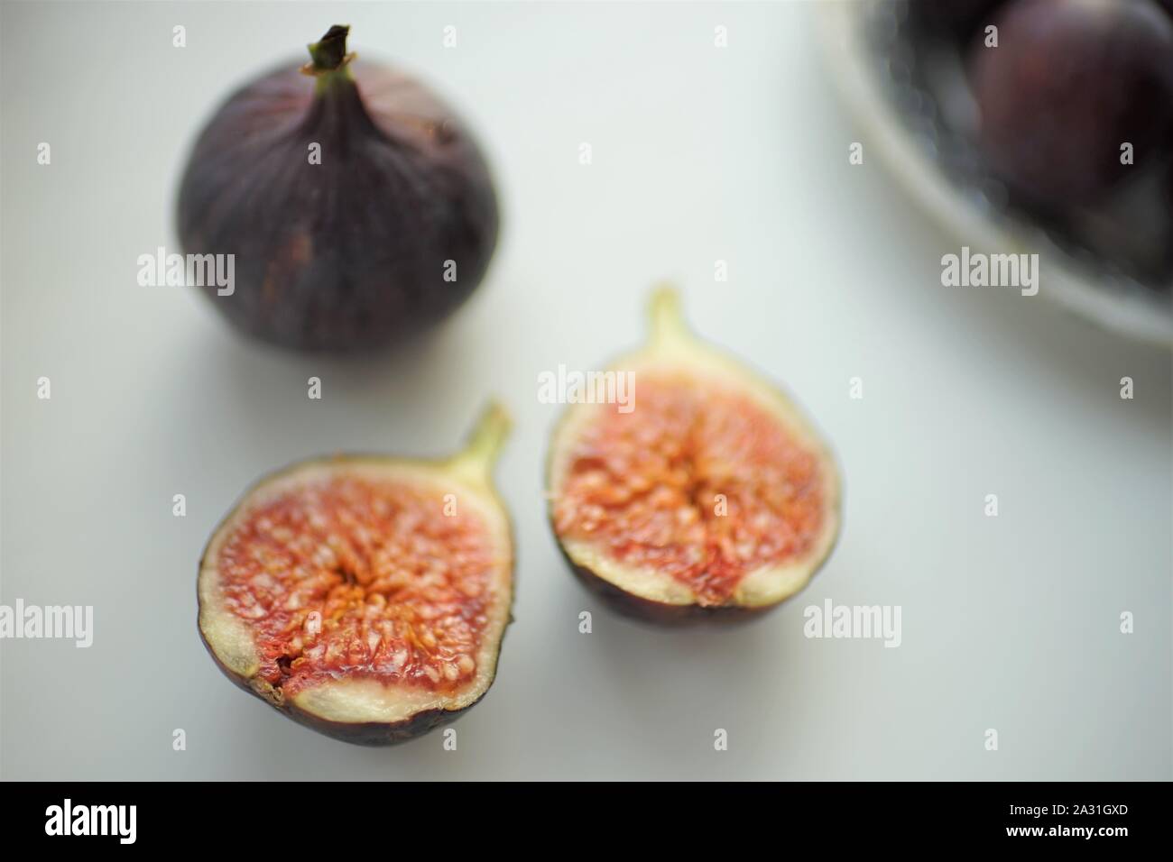 One whole fig and the second cut in half on a white table. Selective focus. Stock Photo