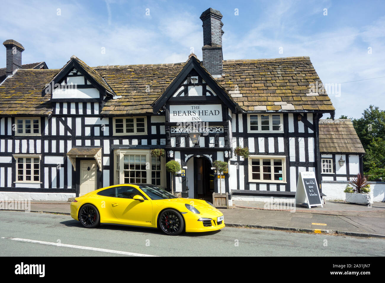 Yellow Porsche sports car parked outside a traditional English black and white half timbered inn public house at Brereton Cheshire England Stock Photo