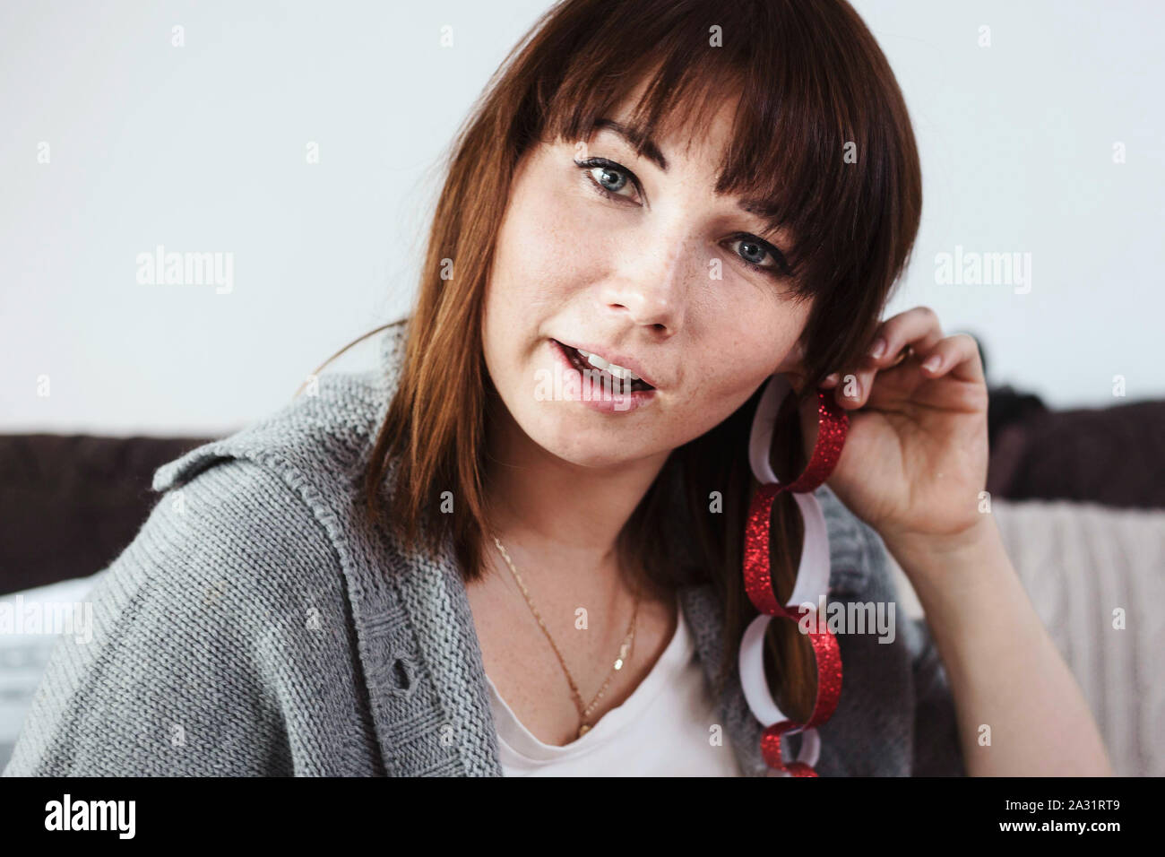 Pretty brunette with bangs, playing with red qlittery paper chain made with her daughter for Christmas. Stock Photo