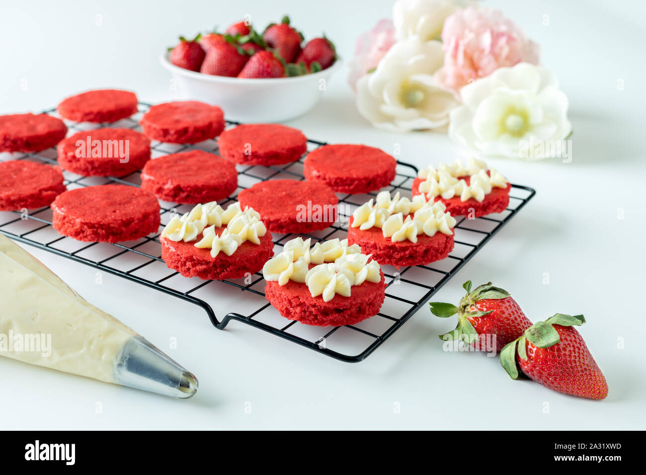 Miniature Red Velvet Cakes with cream cheese frosting and fresh strawberry topping on a cooling rack Stock Photo