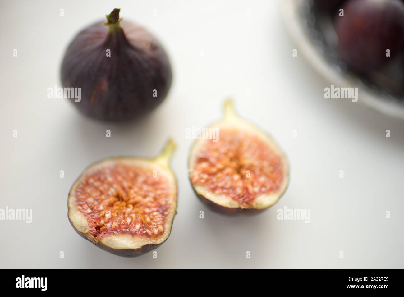 One whole fig and the second cut in half on a white table Stock Photo