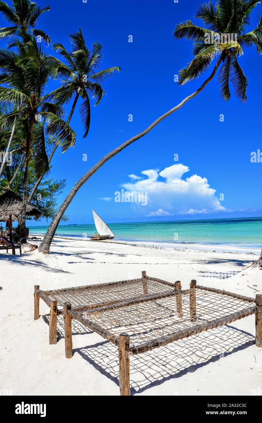 The tropical beach in Zanzibar - crystal clear waters, sun bed and the palm tree. Clear blue sky. Stock Photo