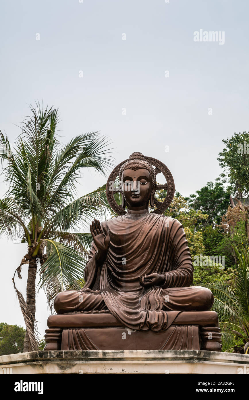 Si Racha, Thailand - March 16, 2019: Closeup of bronze statue of sitting enlightened, compassionate bodhisattva with halo on Ko Loi Island under silve Stock Photo