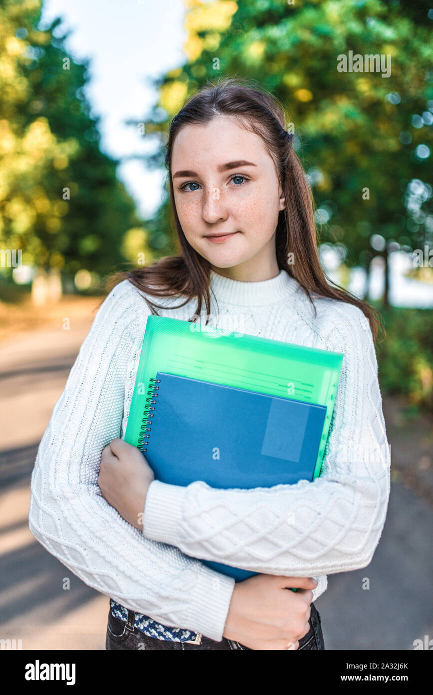 Beautiful teenager girl 1315 years old, stands in summer autumn spring park, holds notebook