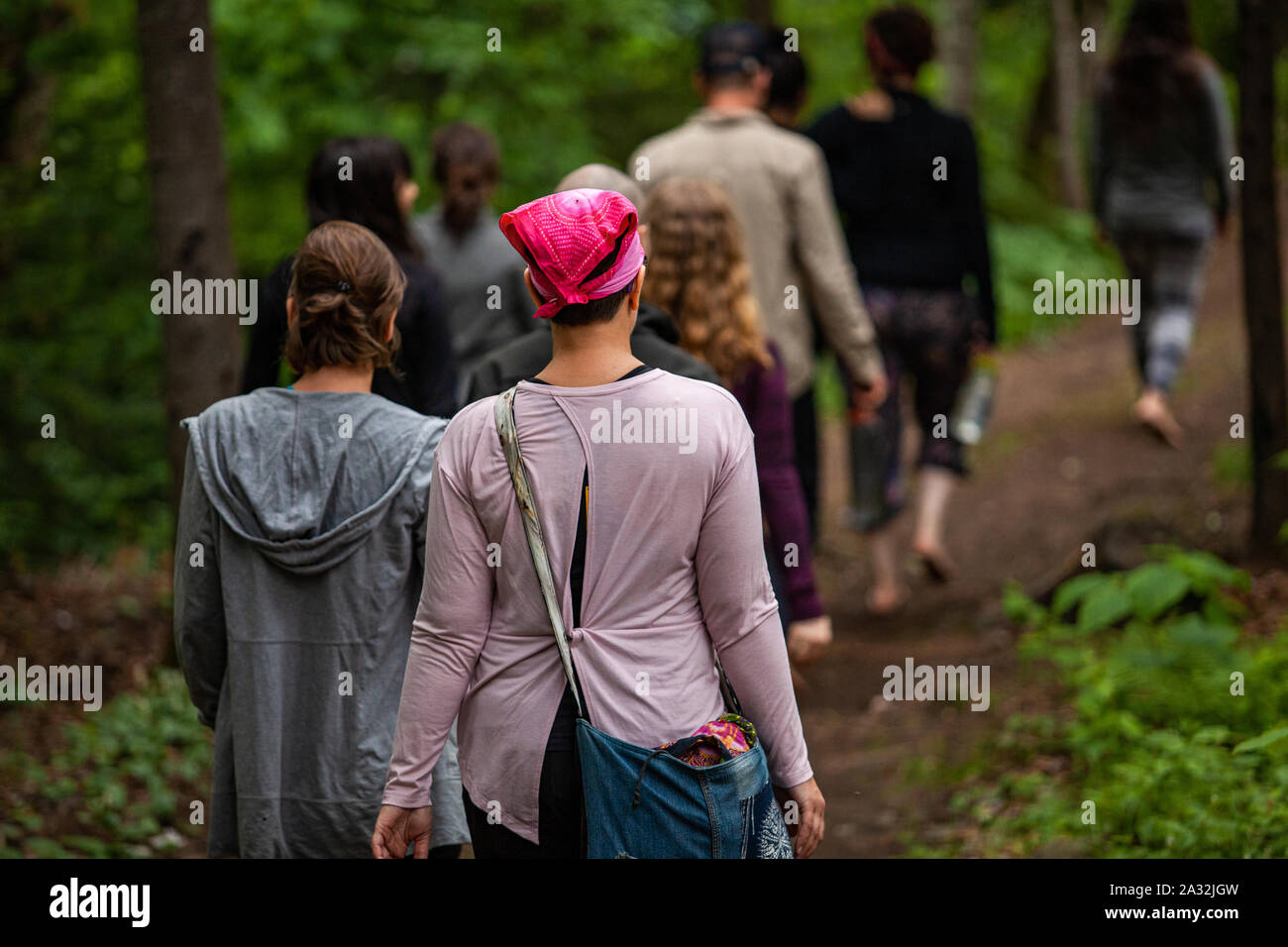 An eclectic mix of people are seen walking barefooted through a sacred woodland trail during a weekend experiencing multicultural activities, with copy space. Stock Photo